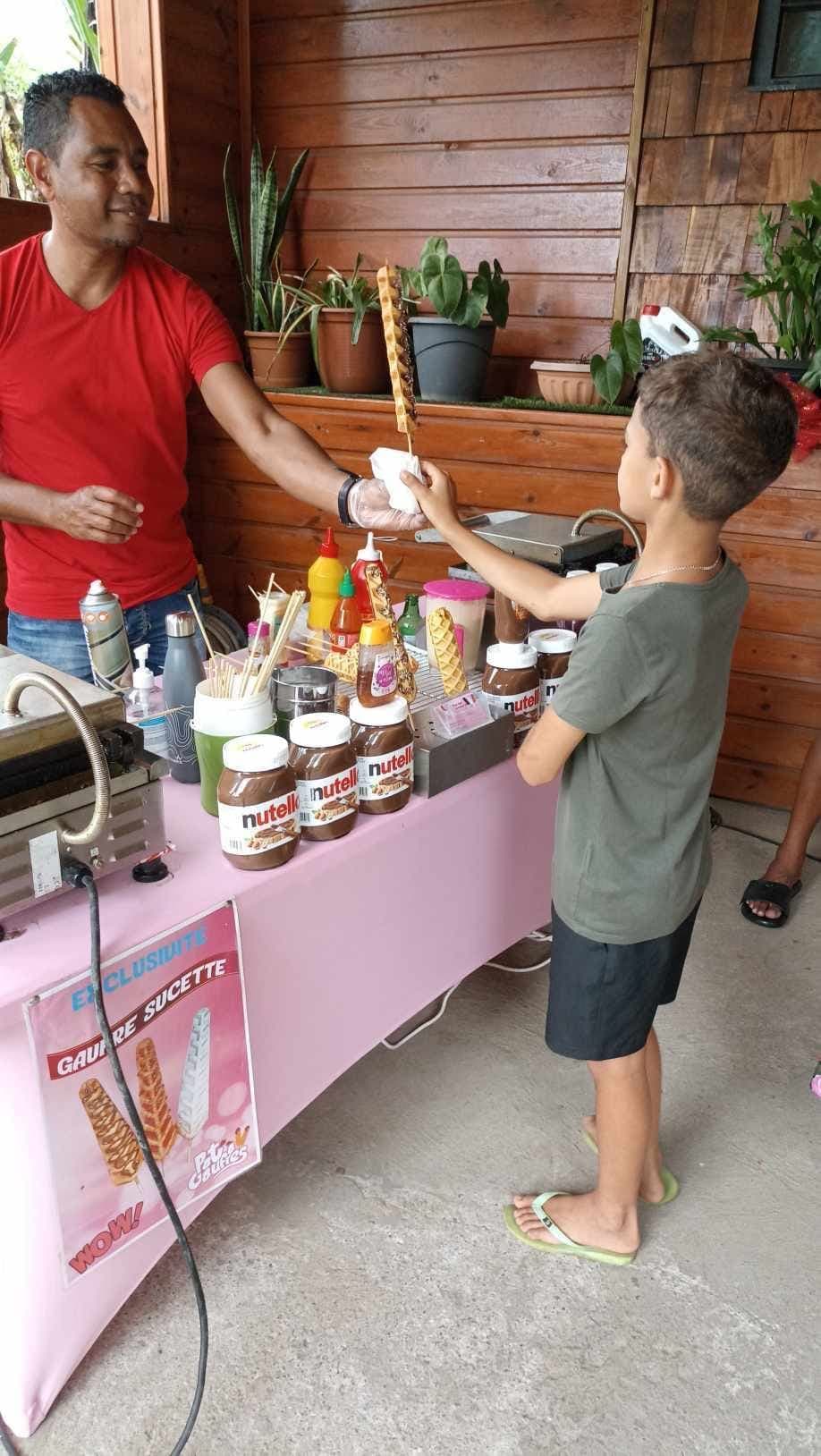 Patrice sert une gaufre sucette à un enfant, préparée en direct sur le stand